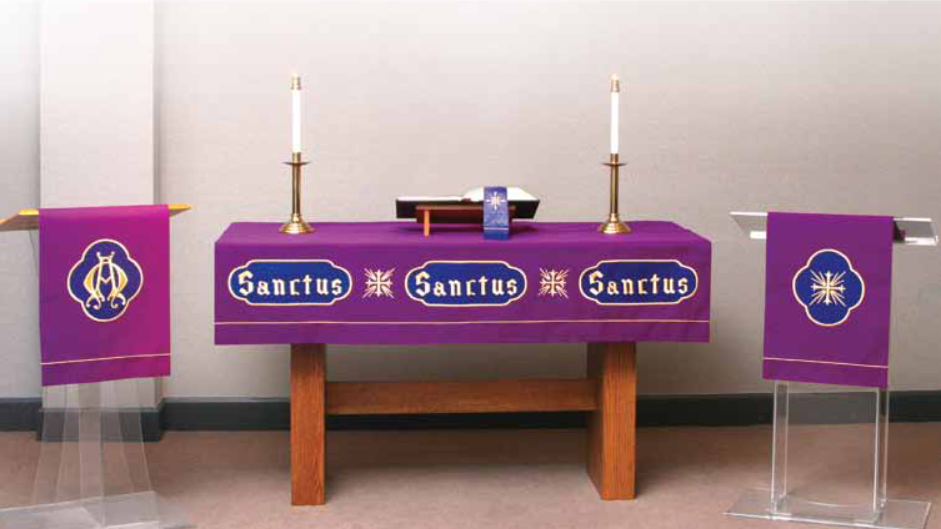 Purple altar table with 'Sanctus' text and lit candles on a plain background